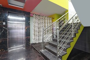 Un ascensor moderno con acabado metálico, al lado de una escalera de mármol con barandilla de metal.