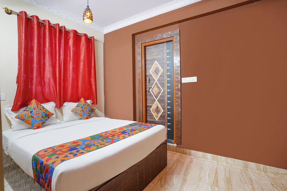 A hotel room with a bed, red curtains, a patterned door, and a tiled floor.