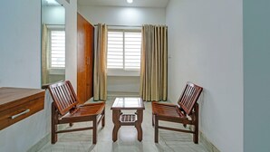 A room with two wooden chairs, a small table, a wooden cabinet, and a window with curtains.