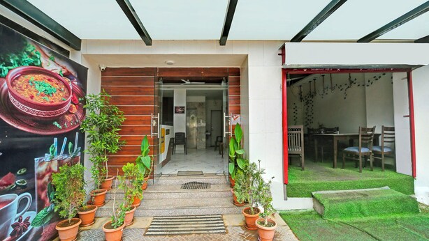 A modern entrance with a glass door, potted plants, and a small outdoor seating area with a green lawn.