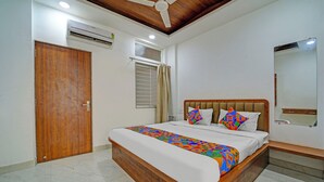 A bedroom with a wooden bed, a ceiling fan, an air conditioning unit, a window with curtains, and a mirror on the wall.