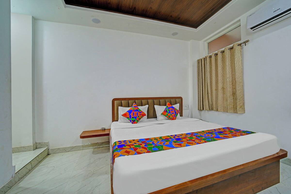 A bedroom with a bed, a wooden headboard, a window with curtains, and a wall-mounted air conditioner.