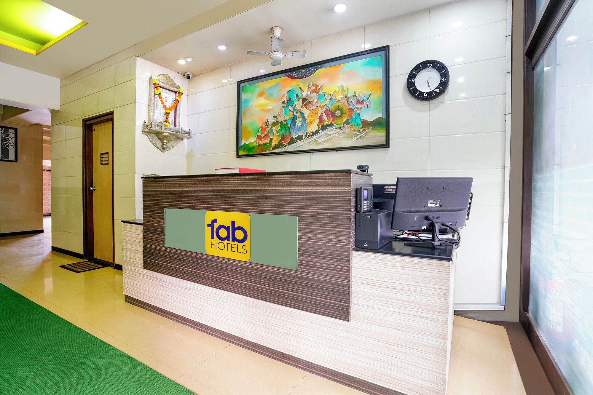A hotel reception desk with a digital display, a clock, and a colorful mural.