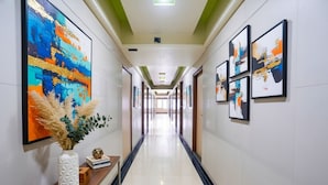 Un long couloir bien éclairé, orné d’œuvres d’art sur les murs, avec une console en bois sur laquelle sont posés un vase et des livres, et un sol carrelé.