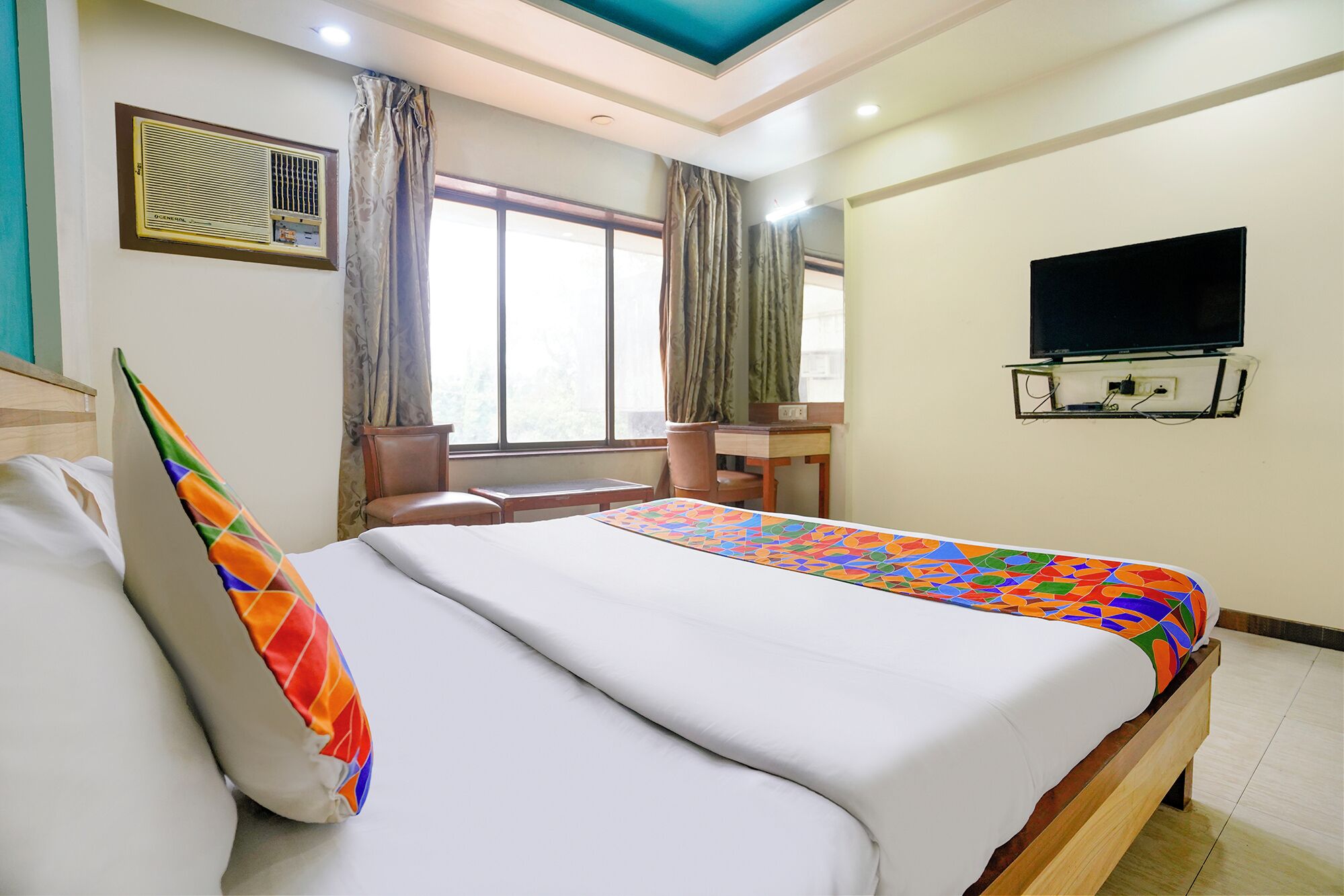 A hotel room with a bed, a desk, a chair, a television, and a window with curtains.