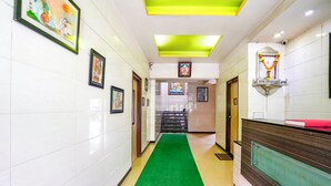 Un hall d’hôtel avec un tapis vert, des œuvres d’art encadrées accrochées aux murs, un comptoir de réception et un escalier.