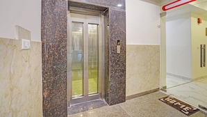 An elevator with a digital display, marble walls, and a glass door. - Fabhotel Golden Rivaah (Ghaziabad)