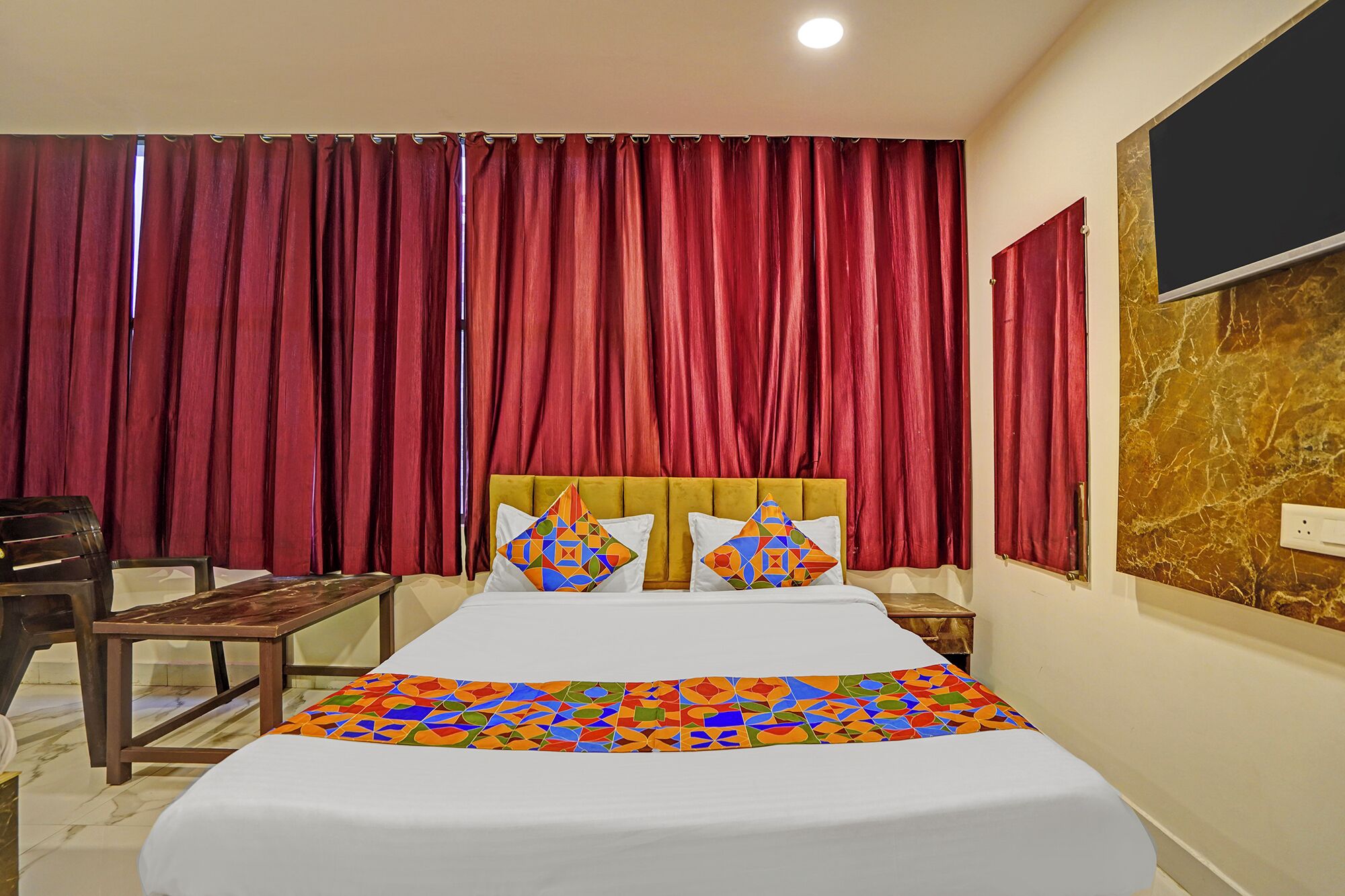A hotel room with a large bed, red curtains, a marble wall, and a wooden nightstand.