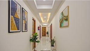 A hallway with framed artwork on the walls, potted plants, and a polished marble floor. - Fabhotel Golden Rivaah (Ghaziabad)