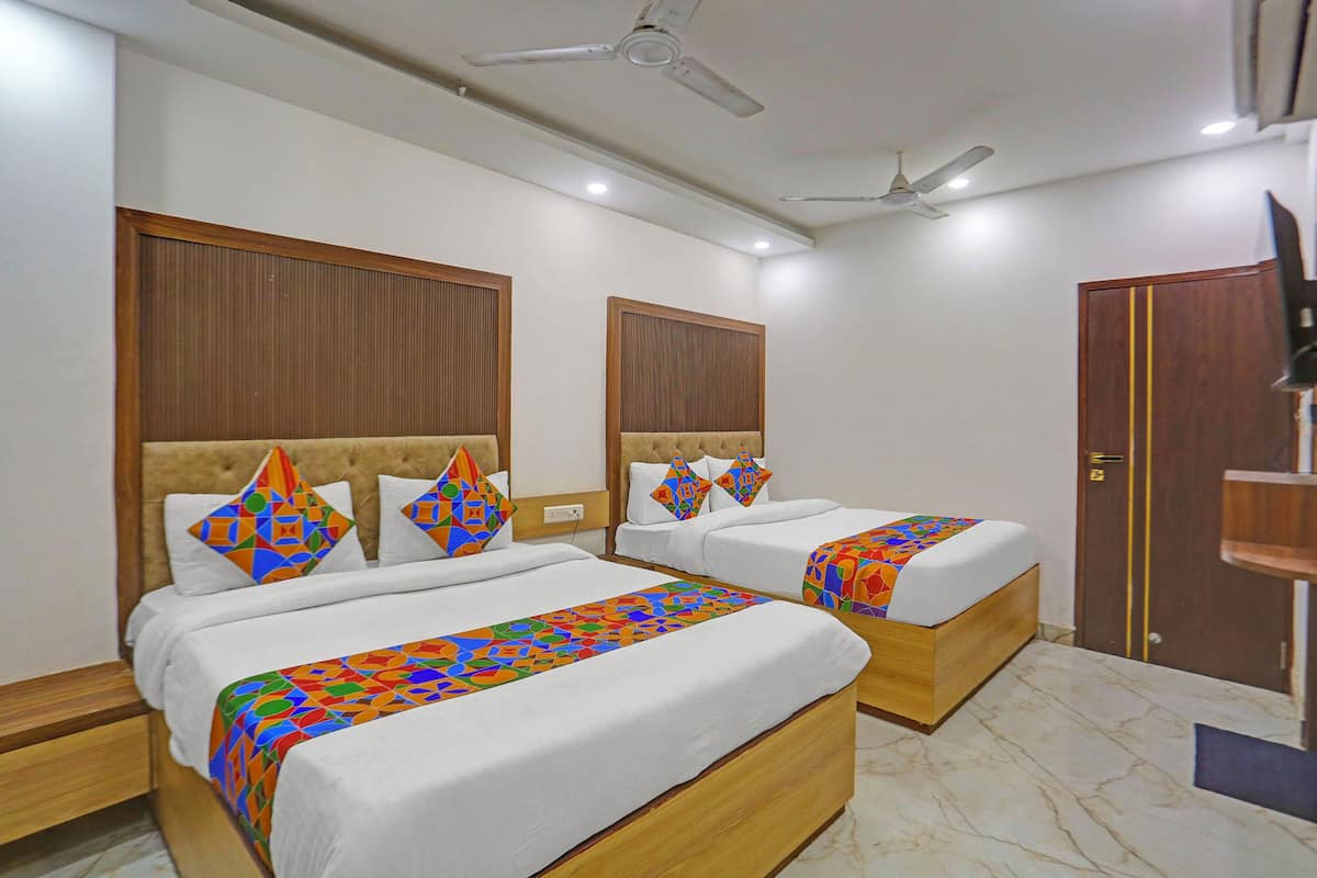 Ein Hotelzimmer mit zwei Betten, Holz-Kopfteilen, weißer Bettwäsche, farbenfrohen Kissen mit geometrischen Mustern, einem Marmorboden und Deckenventilatoren.
