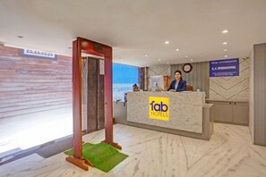 A hotel reception desk with a marble counter, a reception area, and a clock on the wall. - Fabhotel Cg International (New Delhi)