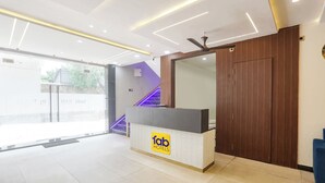 A hotel reception area with a modern design, featuring a reception desk, a large mirror, and a staircase with purple lighting. - Fabhotel Shri Ram Retreat (Mathura)