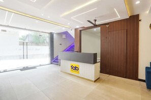 A hotel reception area with a modern design, featuring a reception desk, a large mirror, and a staircase with purple lighting. - Fabhotel Shri Ram Retreat (Mathura)