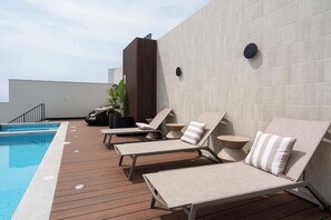 A rooftop pool area with lounge chairs and a modern building in the background.