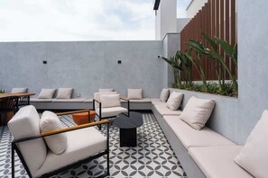 Un área de estar exterior moderna con suelo de estampado geométrico, un sofá, una silla y una mesita.