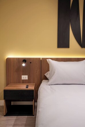 Una habitación de hotel con cabecera de madera, una mesita de noche con control remoto y una decoración abstracta grande en la pared.