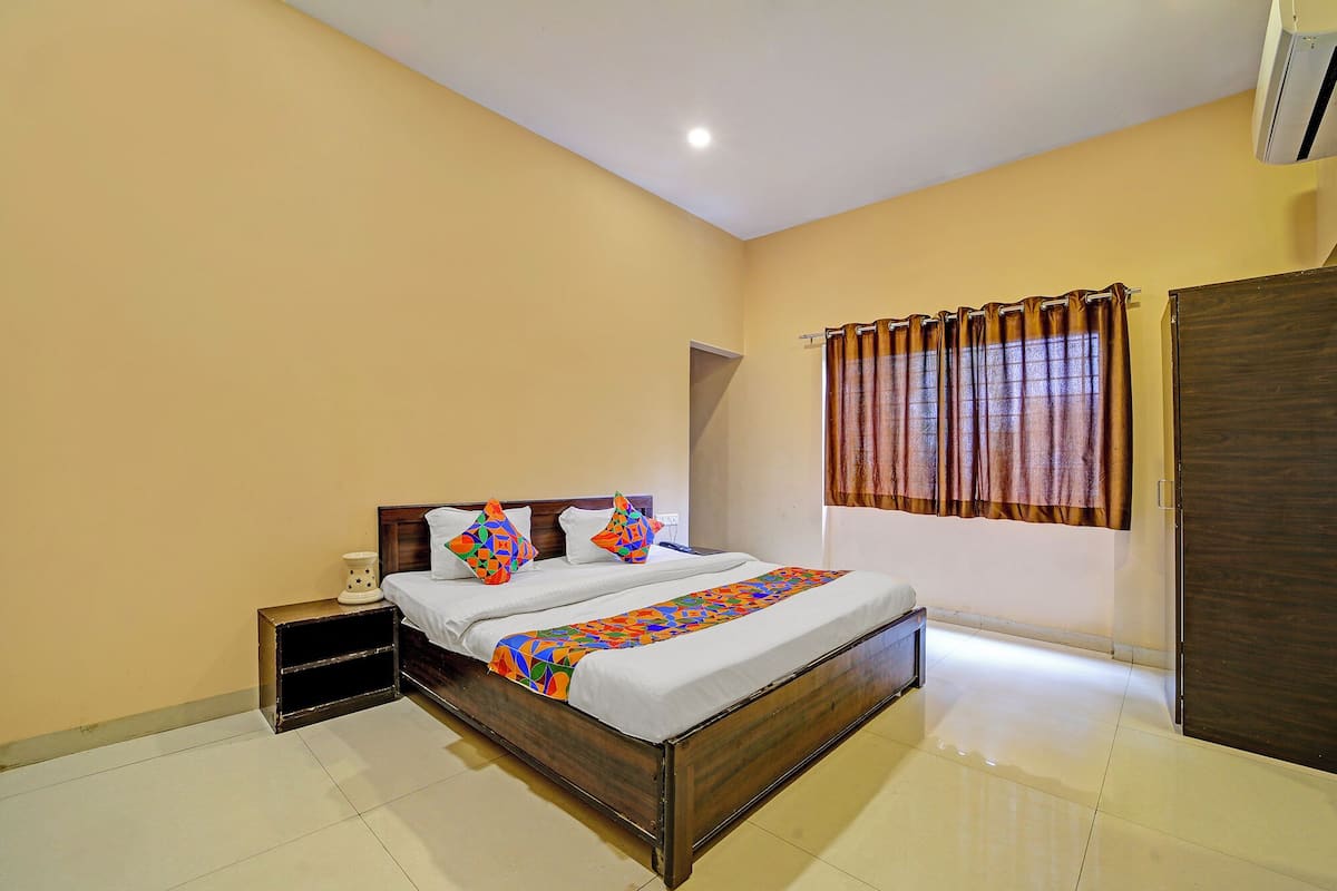 A bedroom with a wooden bed, a nightstand, a bedside table, a window with curtains, and a door.