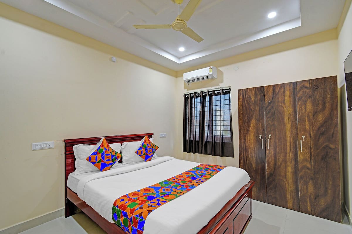 A bedroom with a bed, a wardrobe, a ceiling fan, an air conditioning unit, and a window with curtains.