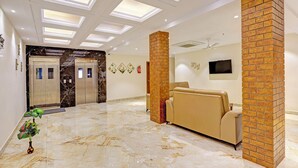 A lobby with a reception area, a sofa, a TV, a fireplace, and an elevator. - Fabhotel Siddarth Prime (Penumuluru)