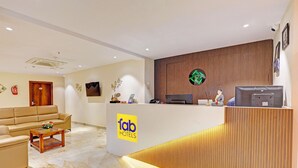 A hotel reception area with a wooden reception desk, a sofa, a coffee table, and a fire extinguisher. - Fabhotel Siddarth Prime (Penumuluru)