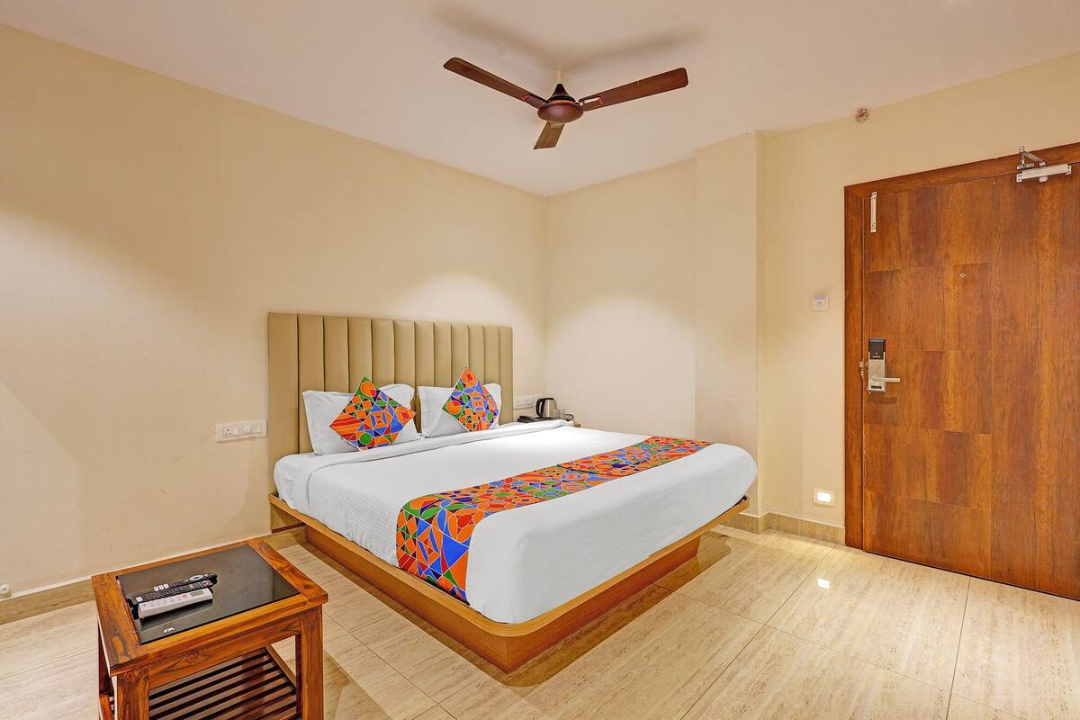 A hotel room with a bed, a wooden nightstand, a ceiling fan, and a wooden door.