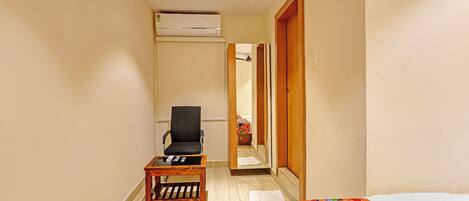 A hotel room with a bed, a chair, a small table, an air conditioning unit, and a door leading to another room.