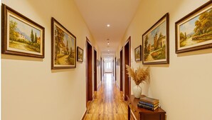 A hallway with wooden flooring, framed paintings on the walls, and a vase with pampas grass on a table. - Fabhotel Siddarth Prime (Penumuluru)