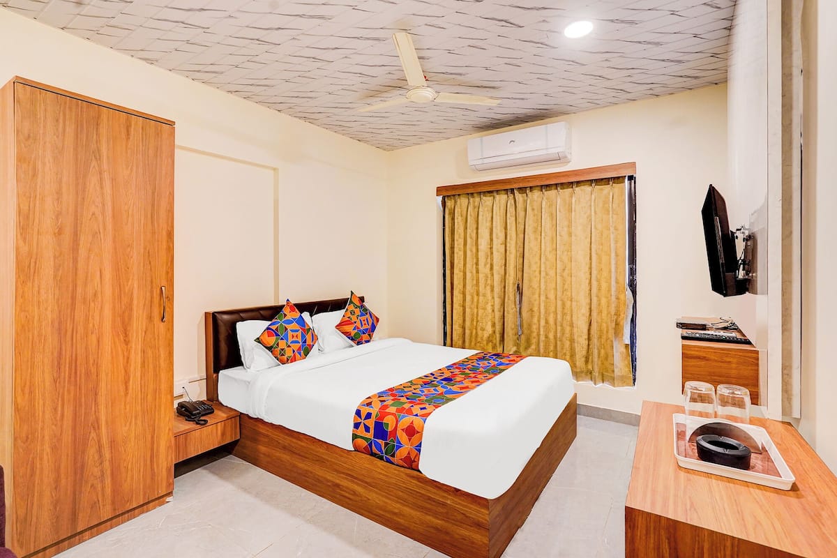 A hotel room with a wooden bed, a desk, a chair, a telephone, and a television.