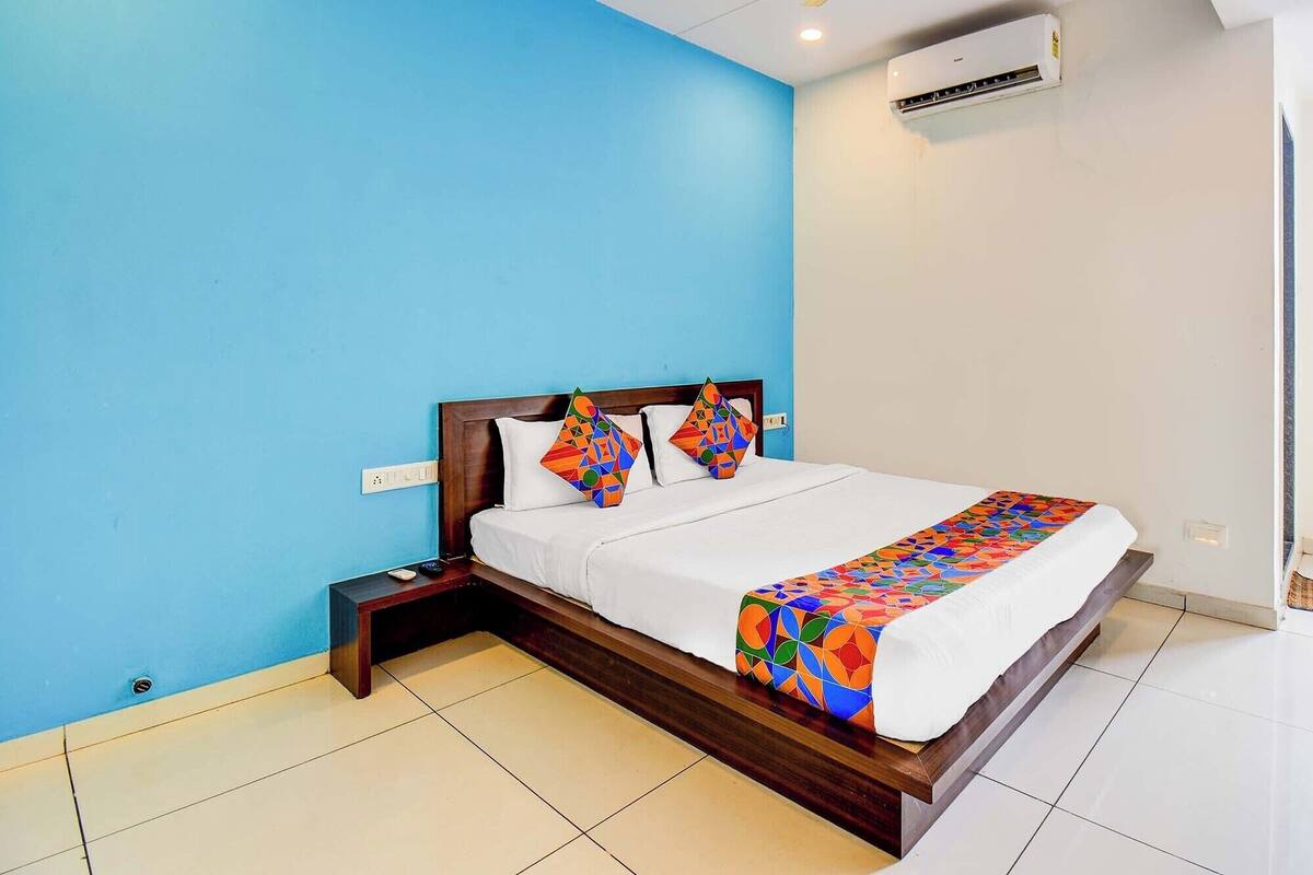 A hotel room with a bed, a nightstand, a wall-mounted air conditioner, and a window.