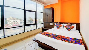 Une chambre d’hôtel moderne avec une grande fenêtre, un lit avec une literie aux couleurs vives et un mur d’accent orange.