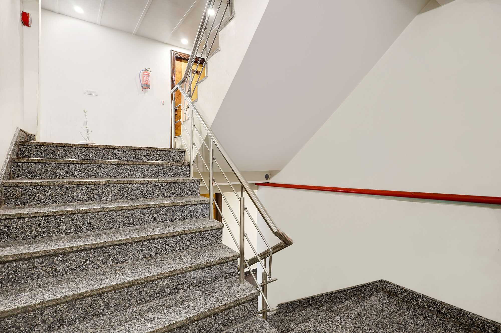 A staircase with granite steps and metal railings, leading to a landing with a red handrail.