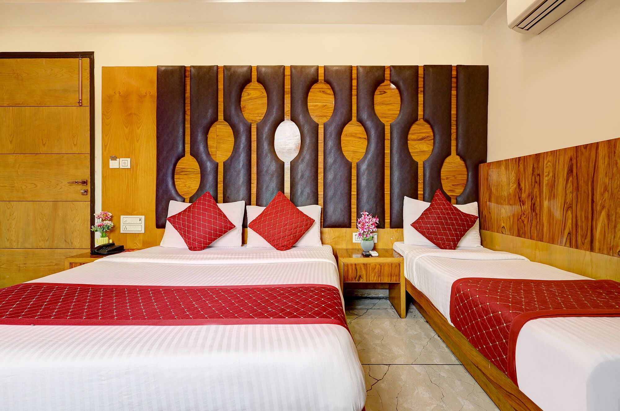 A hotel room with two beds, a wooden headboard, and a nightstand with a vase of flowers.