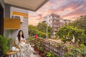 A balcony with a person seated, surrounded by potted plants and a table with a teapot. - FabHotel Comfy Cottage - 700 Meters From Artemis Hospitals, Sector 51 (Gurugram)