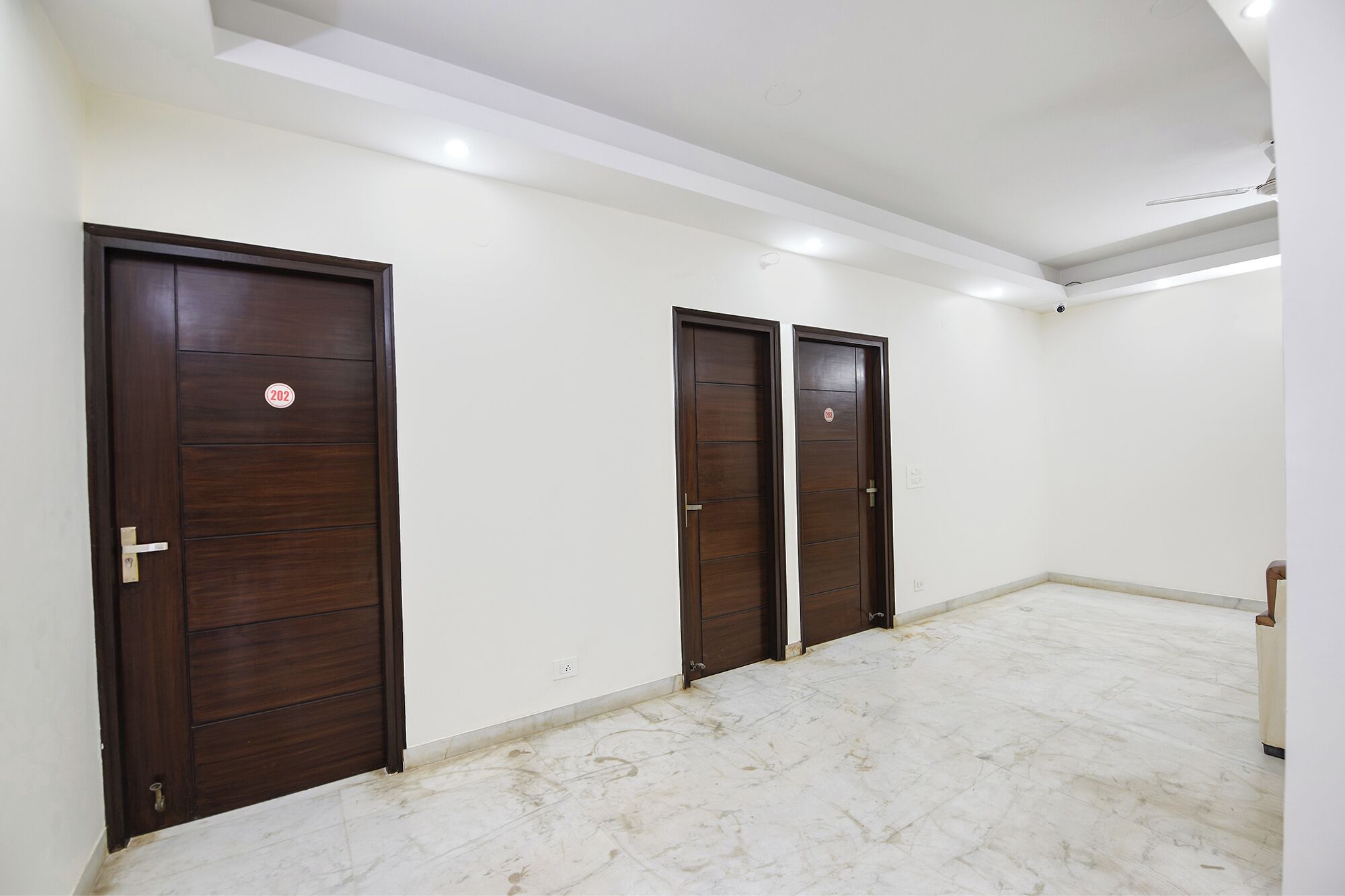 A room with three dark wooden doors, white walls, and a marble floor.