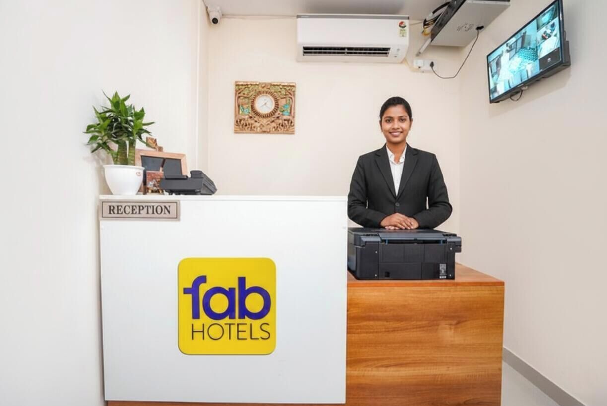 Una recepción con un cartel que dice 'fab hotels', una planta, un reloj y un televisor montado en la pared.