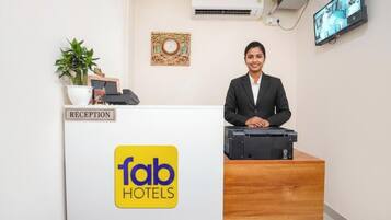 Una recepción con un cartel que dice 'fab hotels', una planta, un reloj y un televisor montado en la pared.