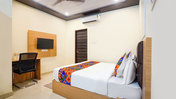 A modern hotel room with a bed, a desk, a chair, a television, and an air conditioning unit. - FabHotel Paramhans Guest House - Nr. Sant Ravidas Ghat (Varanasi)