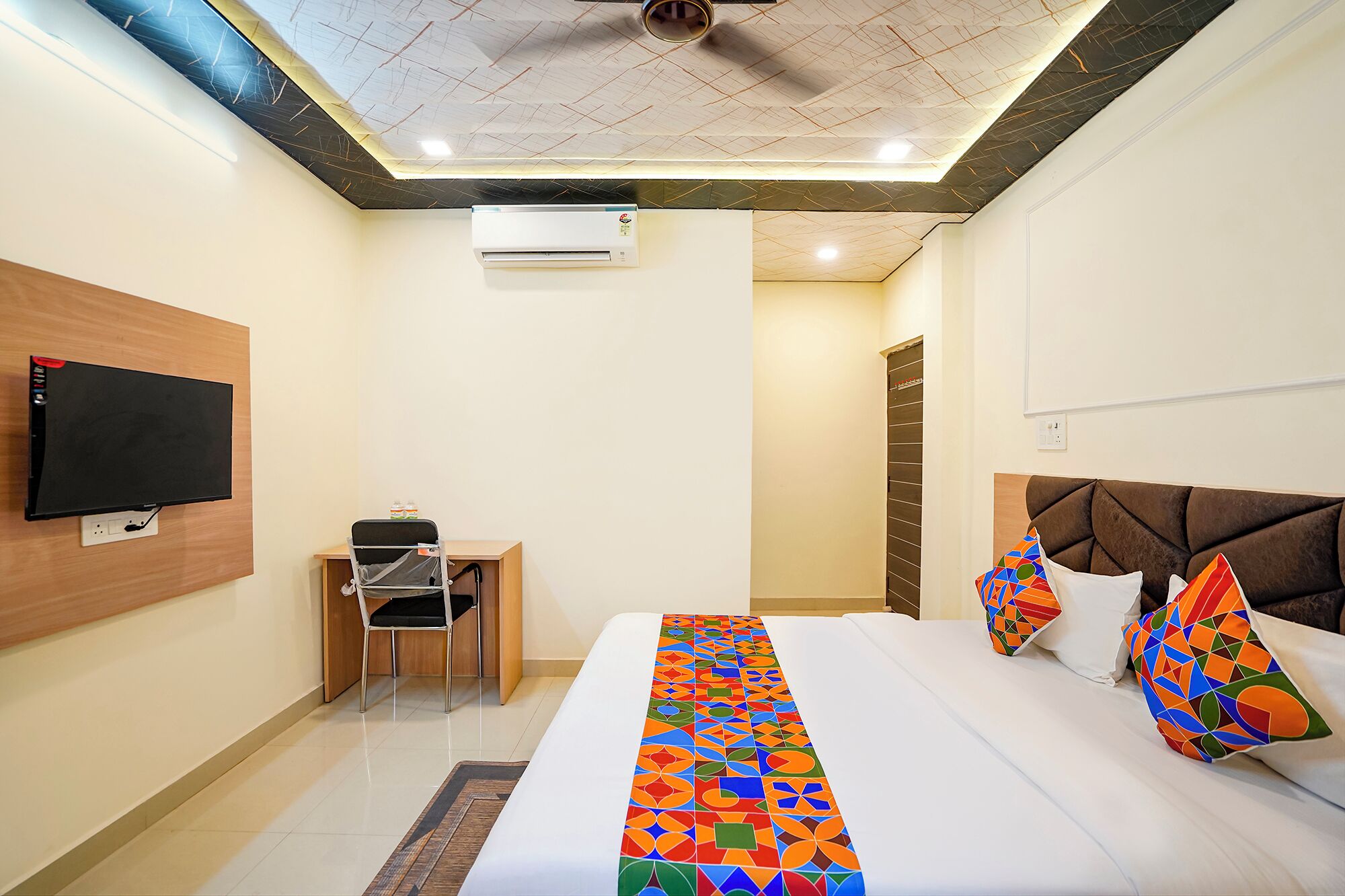 Habitación de hotel con cama, escritorio, silla, televisor y aire acondicionado.