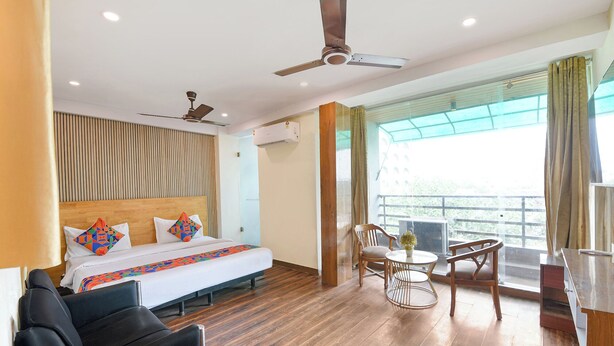 Quarto de hotel com cama, escrivaninha, cadeira, sofá, ventoinha no teto e janela com vista.