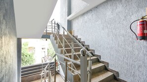 Escadaria com corrimão de metal, extintor fixado na parede e vista para o verde lá fora.
