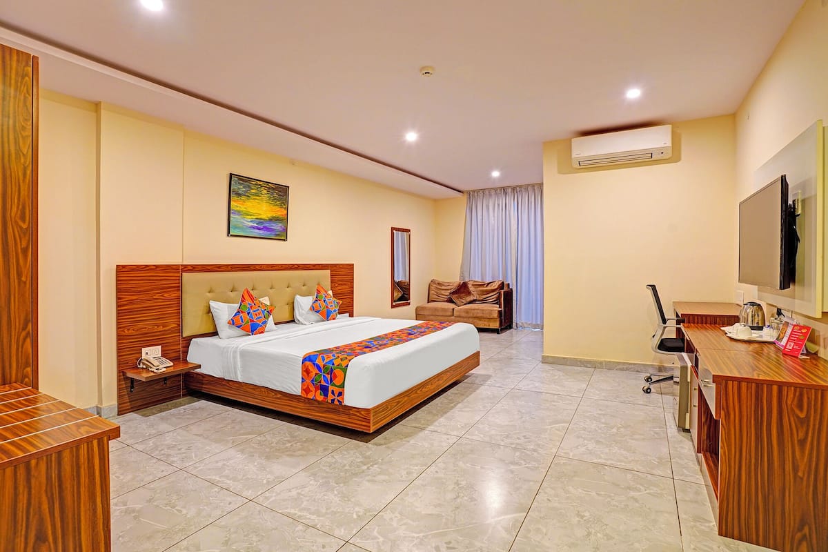 A hotel room with a large bed, a desk, a chair, a TV, and an air conditioner.