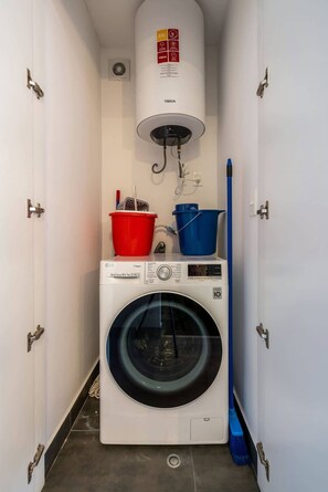 Ein kleiner Waschraum mit einer Waschmaschine mit Frontlader, einem Dampfbügeleisen und einem blauen Wischmopp.
