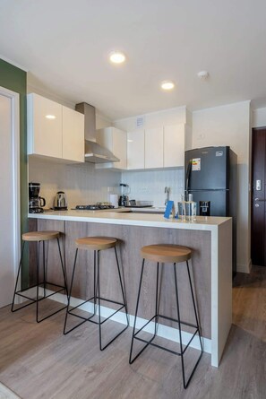 A modern kitchen with a central island, bar stools, and a refrigerator.