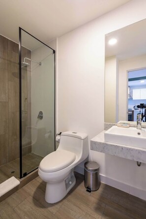 Une salle de bain moderne avec une douche à parois de verre, des toilettes, un lavabo doté d’un plan de travail en marbre et une poubelle.