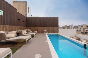 A rooftop pool area with lounge chairs, a pool, and a view of the cityscape.