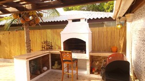 An outdoor patio with a brick fireplace, a wooden chair, and a grill. - Tropical Comfort: Your Curaçao Retreat Awaits (Willemstad)