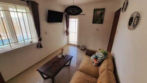 A living room with a sofa, a wooden coffee table, a TV mounted on the wall, and a window with curtains. - Tropical Comfort: Your Curaçao Retreat Awaits (Willemstad)