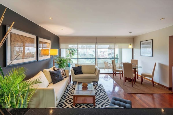 A modern living room with a sofa, coffee table, and dining area with chairs. - Geko | Inviting 2BR in San Isidro w/ Park Views (San Isidro)