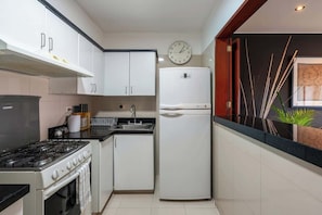 A compact kitchen with white cabinets, a stove, a refrigerator, and a clock on the wall. - Geko | Inviting 2BR in San Isidro w/ Park Views (San Isidro)