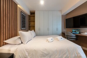 Een hotelkamer met een bed, een bureau met een computer, een televisie en een kledingkast.